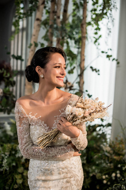 Woman in a sparkling dress holding flowers in an outdoor setting with greenery.