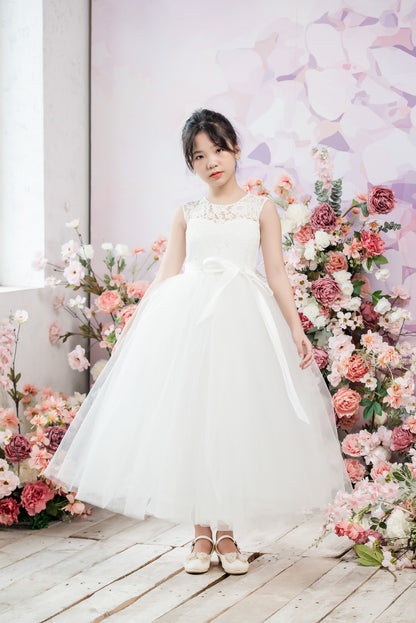 Young girl in a white dress standing in front of a floral backdrop