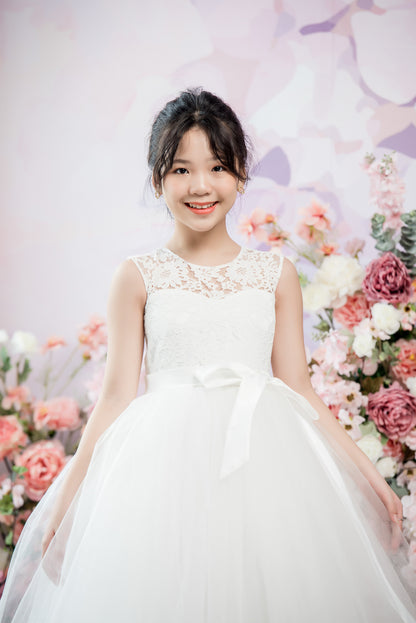 Young girl in a white dress standing in front of a floral backdrop
