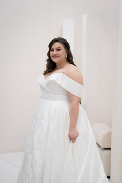 Woman wearing a white off-shoulder gown against a plain background