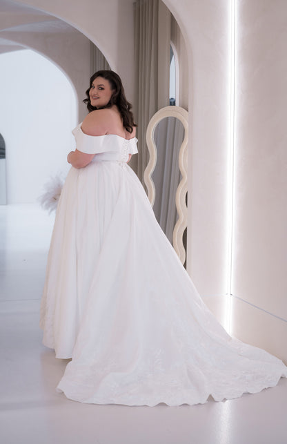 Woman in a white off-shoulder wedding dress standing in a softly lit room