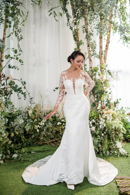 Woman in a white wedding dress standing in a decorated outdoor setting with greenery and flowers.