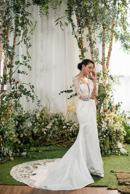 Woman in a white wedding dress standing in front of a floral and greenery arch.
