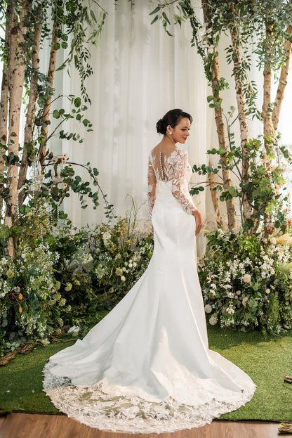 Woman in a white wedding dress standing in a decorated outdoor setting with flowers and trees.