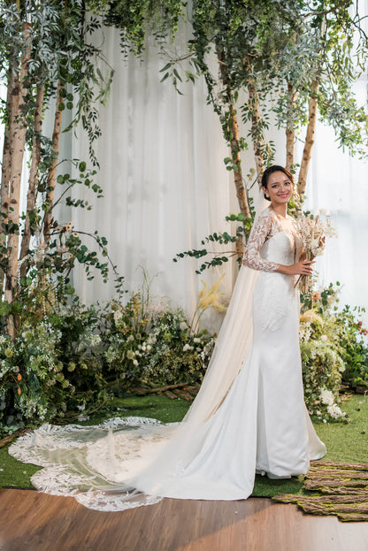 Woman in a white dress standing in front of a floral and tree archway.