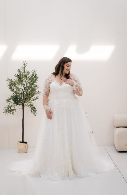 Woman in a white wedding dress standing in a minimalistic room with a plant