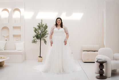 Woman in a white wedding dress standing in a bright, minimalistic room with a plant and furniture