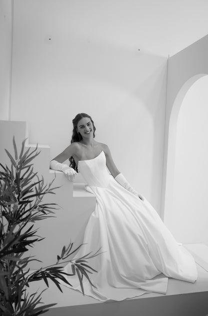 Woman in a white wedding dress standing in a minimalistic room with a plant.