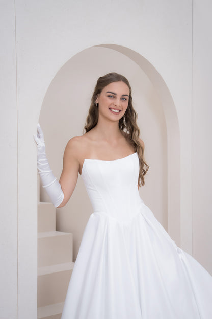 Woman in a white wedding dress standing in a softly lit room with a white archway.