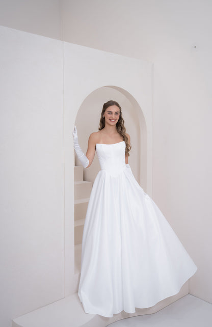 Woman in a white strapless gown standing in a minimalistic room with a white wall and staircase.