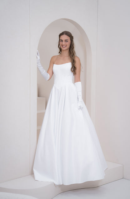 Woman in a white wedding dress standing in a softly lit room.