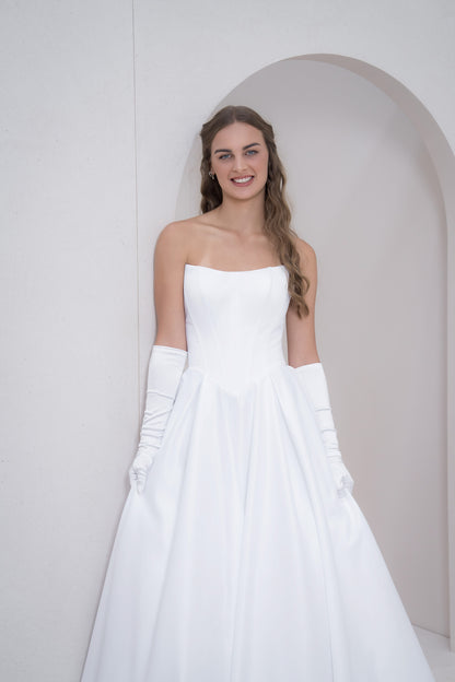 Woman in a white strapless dress with long white gloves against a plain background
