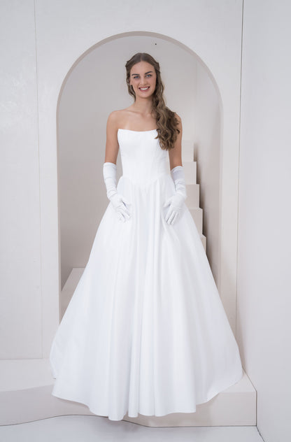 Woman in a white strapless gown with gloves standing in a minimalistic setting.