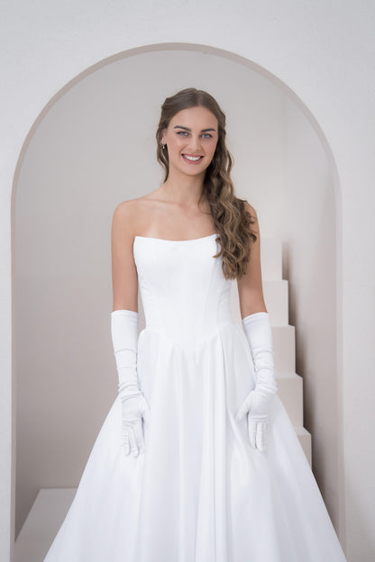 Woman in a white strapless dress with long gloves standing in a minimalistic setting.