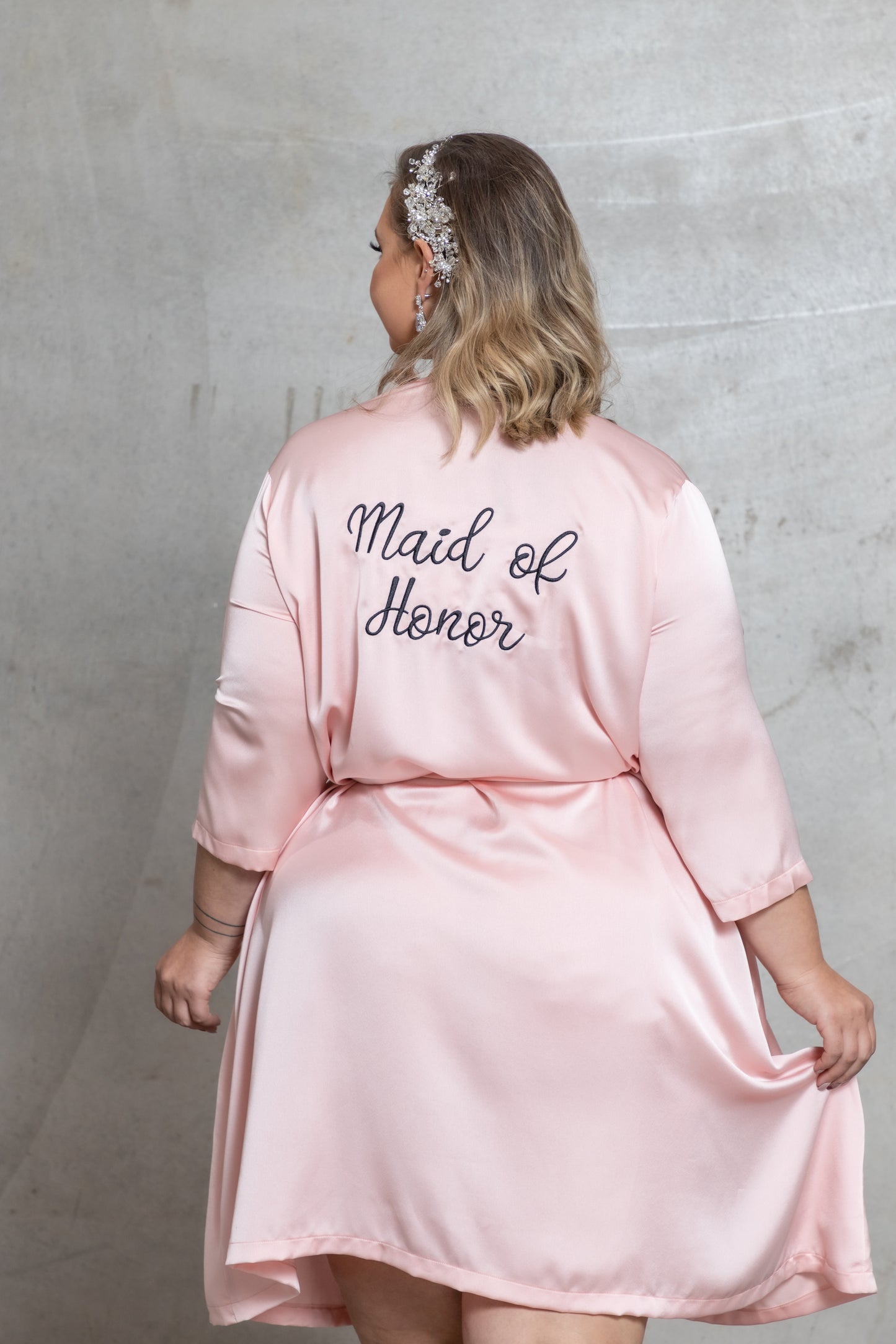 Woman wearing a pink 'Maid of Honor' robe against a gray background