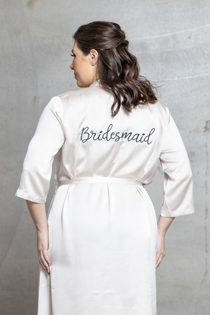 Woman wearing a white 'Bridesmaid' robe against a gray background