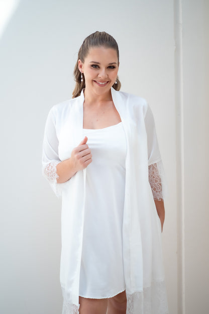 Woman wearing a white dress with a matching cardigan against a plain background