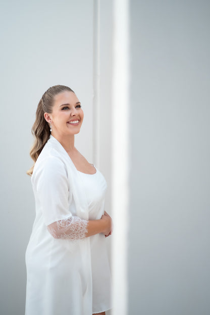 Woman in a white outfit standing in a doorway with a plain background
