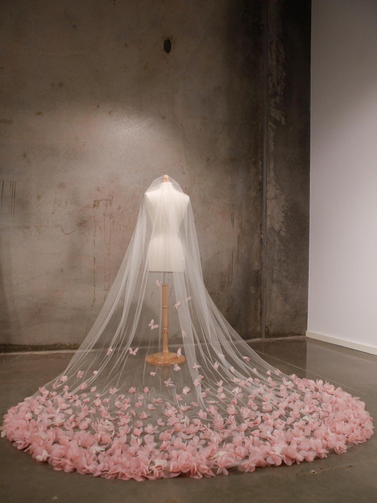 Veil with pink flower petals on a mannequin against a plain wall.