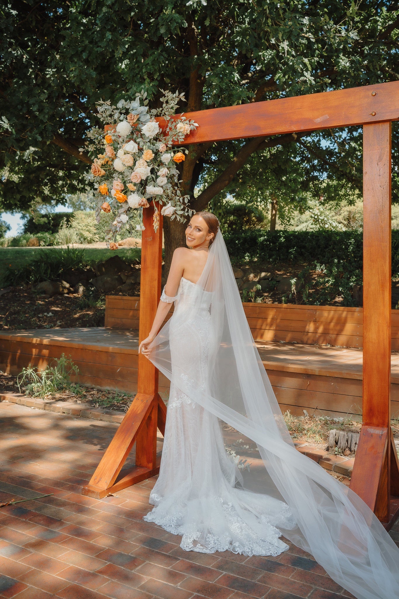 Bride in lace gown under floral arch in garden setting