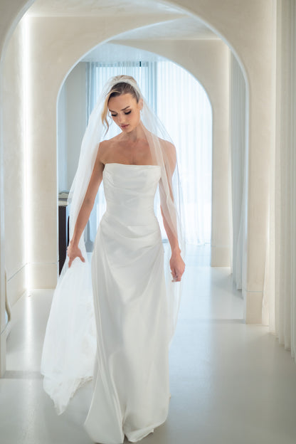 Woman in a white wedding dress standing in a bright, minimalistic room with arched doorways.