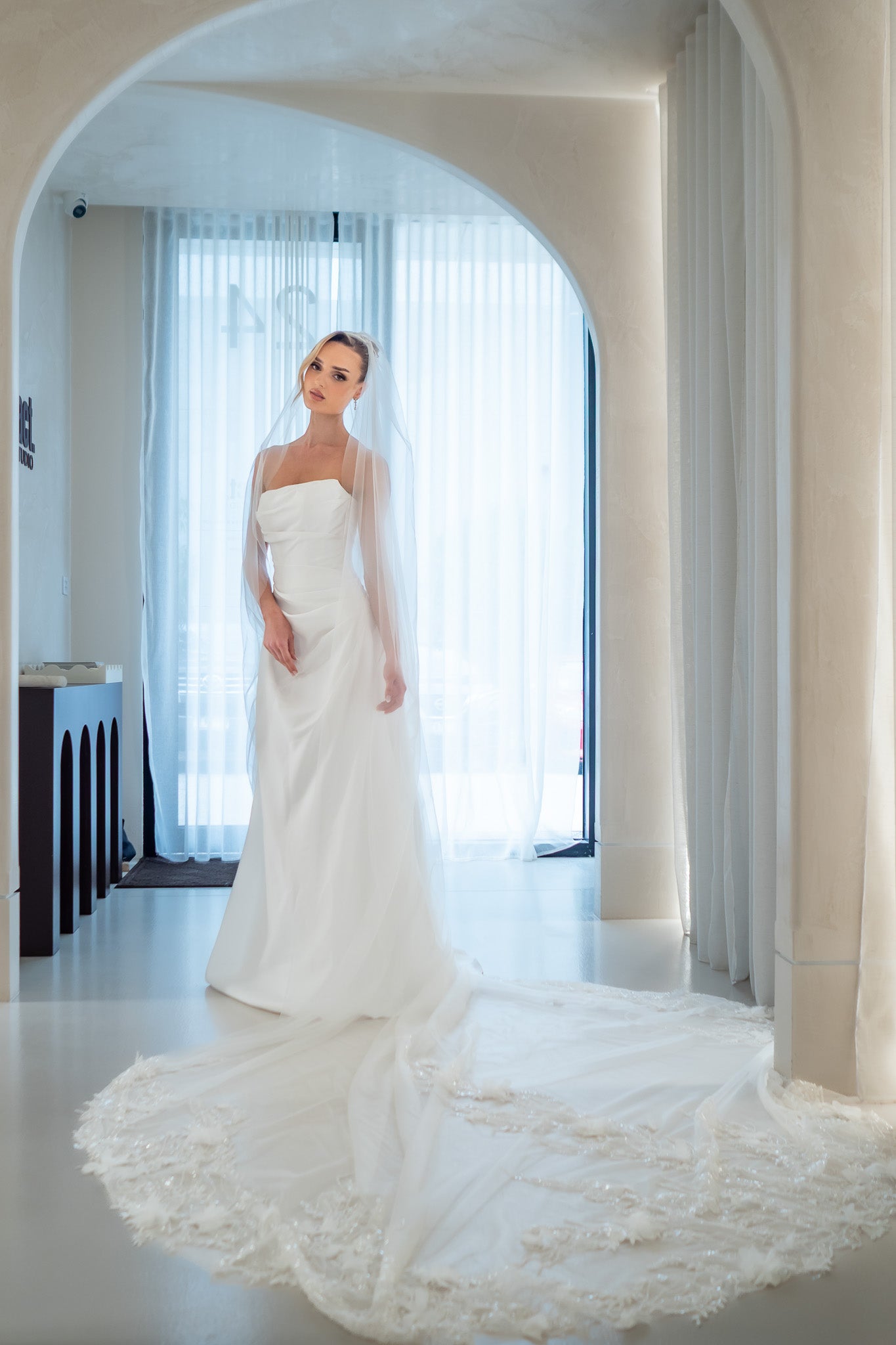 Woman in a white wedding dress standing in a room with large windows.