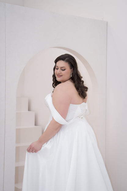 Woman in a white wedding dress standing against a light-colored wall