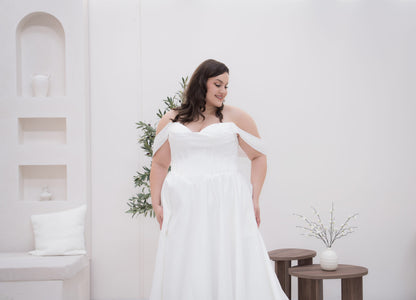 Woman in a white off-shoulder dress standing in a minimalistic room with white walls and furniture