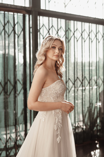 Woman in a strapless wedding dress with intricate detailing standing in front of decorative metal gates.