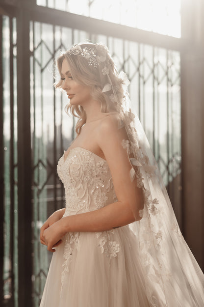 Bride in an elegant wedding dress with a floral headpiece and veil, standing in front of a decorative metal gate.