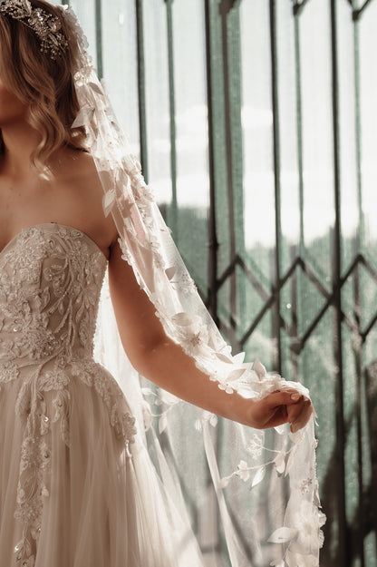 Woman in a wedding dress with a long veil standing in front of a decorative metal gate.