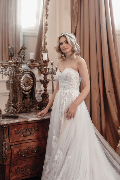 Woman in a white wedding dress standing in an elegant room with a clock and curtains