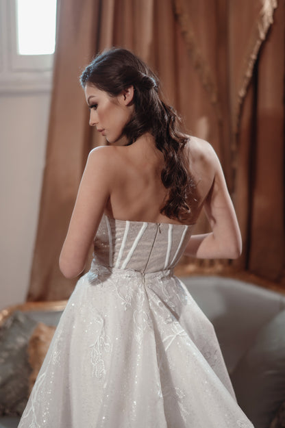 Woman in a sparkly silver dress standing in a room with curtains.