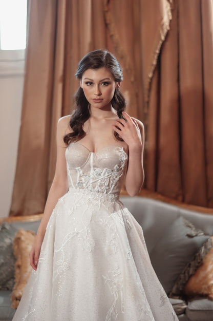 Woman in a white wedding dress standing in a room with brown curtains.