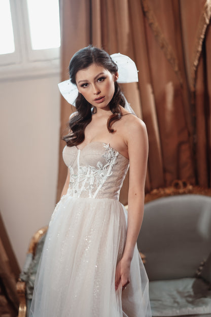 Woman in a white wedding dress with intricate detailing standing in a decorated room.