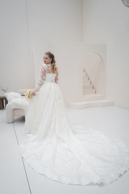Woman in a white wedding dress standing in a minimalistic room with a white couch and wall.