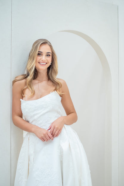 Woman in a white strapless dress standing against a plain background