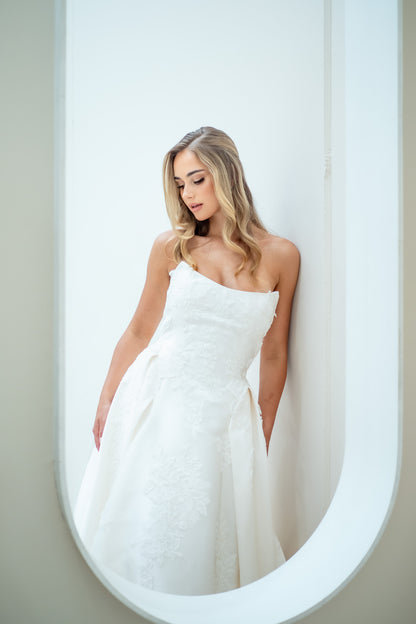 Woman in a white strapless dress standing in front of a mirror.