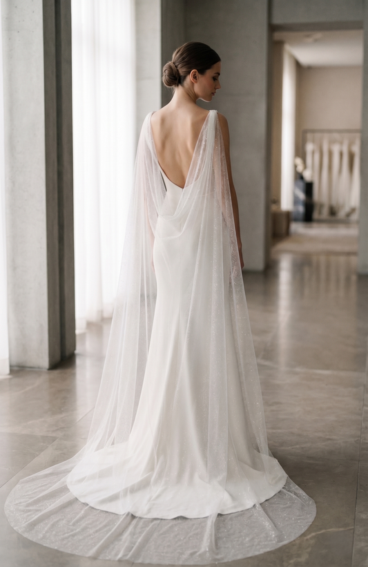 Woman in a white wedding dress with a long train standing in a softly lit room.