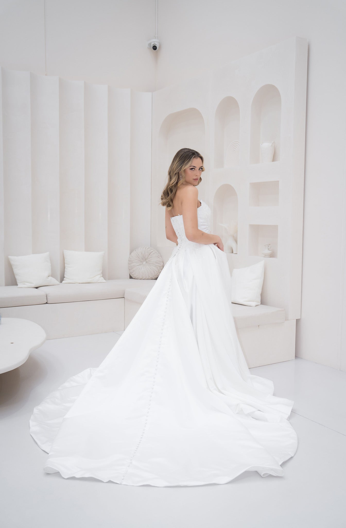 Woman in a white wedding dress standing in a minimalistic room with white decor.
