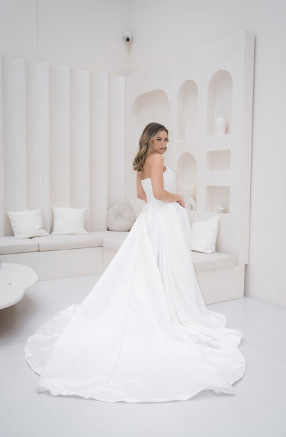 Woman in a white wedding dress standing in a minimalistic room with white decor.