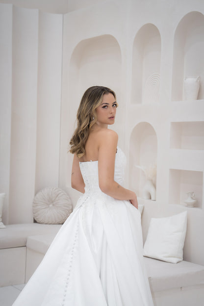 Woman in a white strapless dress standing in a minimalistic room with white walls and furniture.