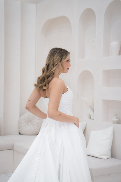 Woman in a white strapless dress standing in a minimalistic room with white walls and furniture.