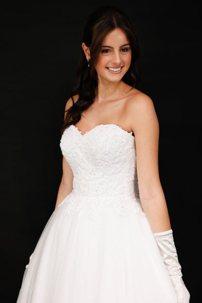Woman in a white strapless dress with long gloves against a black background