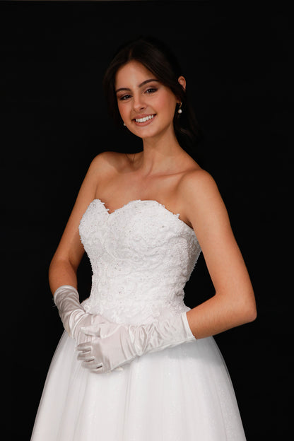 Woman wearing a white strapless dress and gloves against a black background