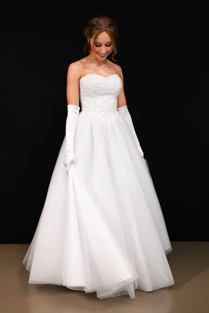 Woman wearing a strapless white wedding dress with gloves on a black background