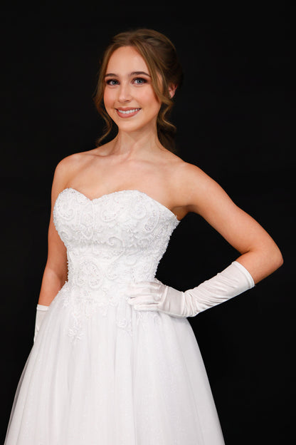 Woman in a white strapless gown with lace details and white gloves against a black background