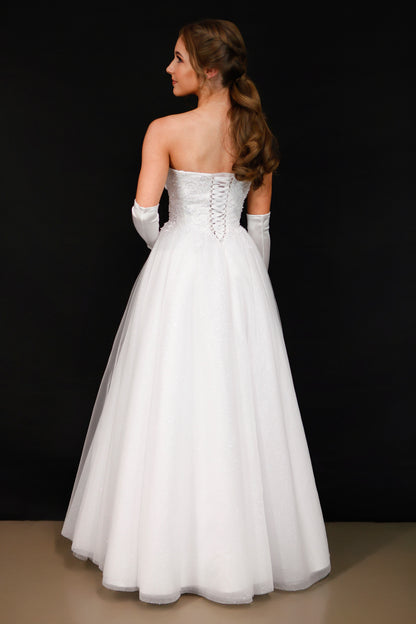 Woman wearing a white strapless wedding dress with lace detailing on a black background