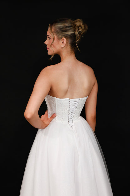 Woman wearing a white strapless gown with a corset back against a black background