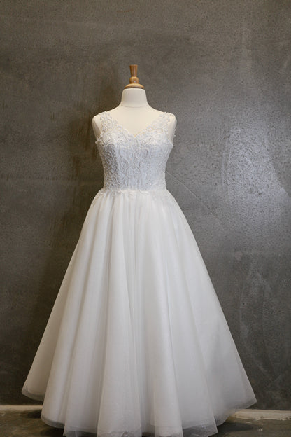 White lace wedding dress on a mannequin against a gray textured wall